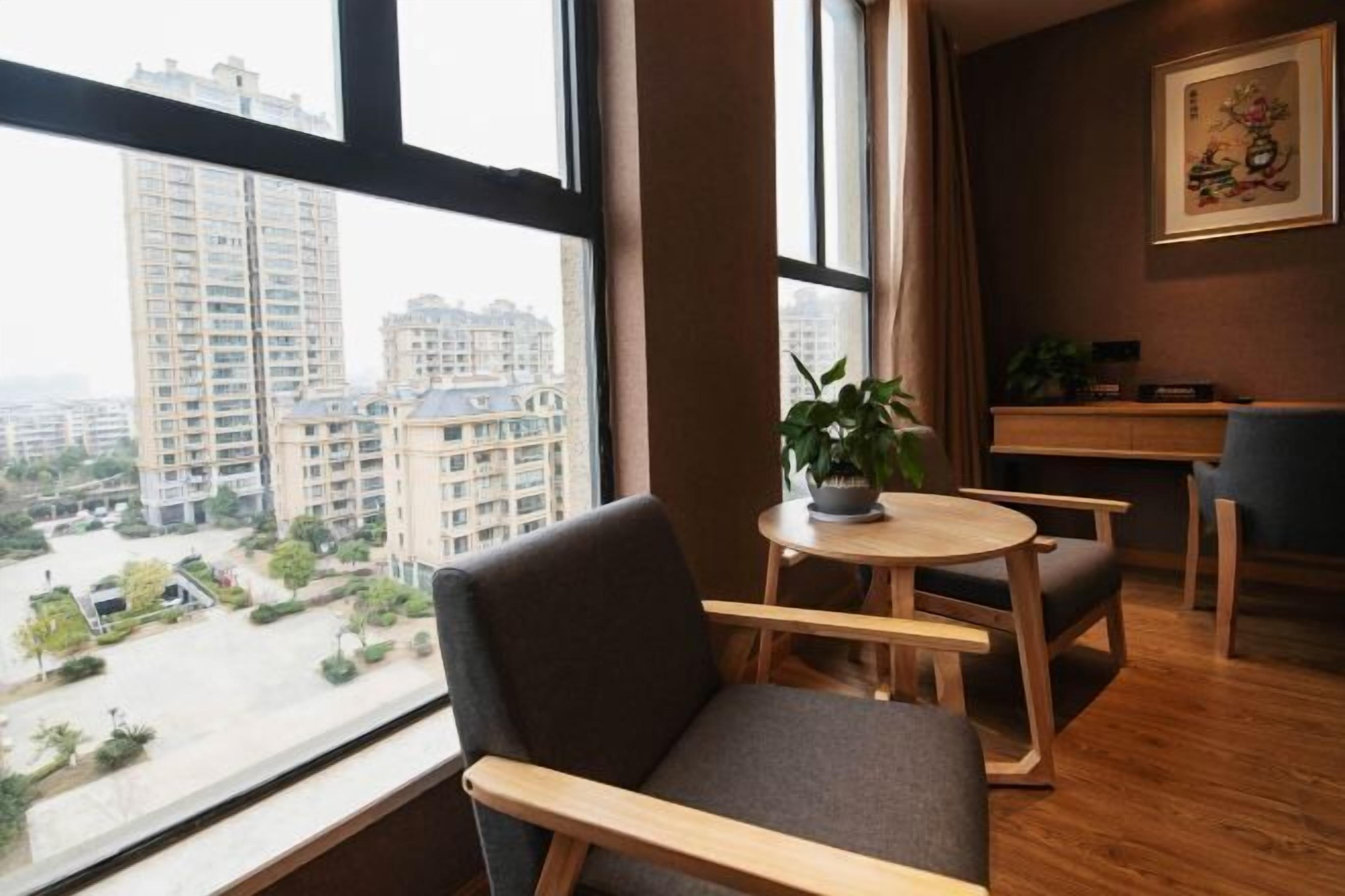 A modern room with a view of high-rise buildings, a small round table with a plant, and a grey sofa.