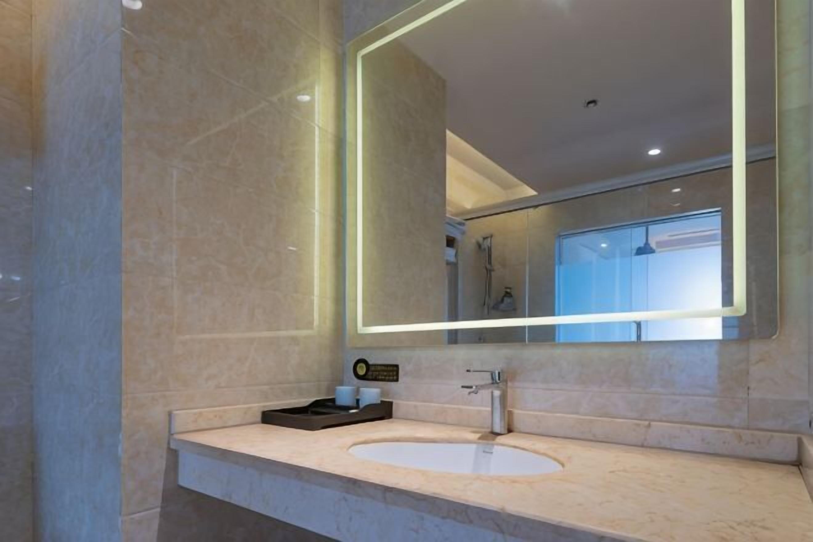 Une salle de bain moderne avec un lavabo en marbre, un grand miroir et un appareil portatif posé sur le comptoir.