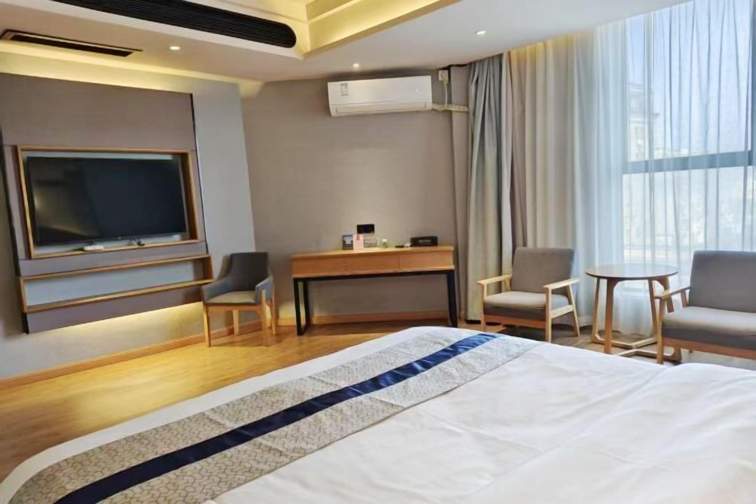 Ein Hotelzimmer mit einem großen Bett, einem Schreibtisch, einem Stuhl, einem Fernseher und einer Klimaanlage.