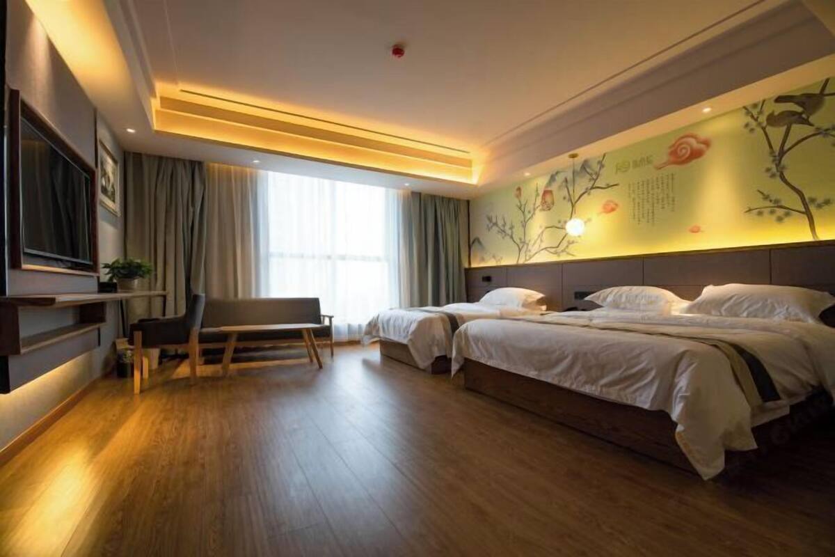 A hotel room with a bed, a desk, a chair, a TV, and a wall with artwork.
