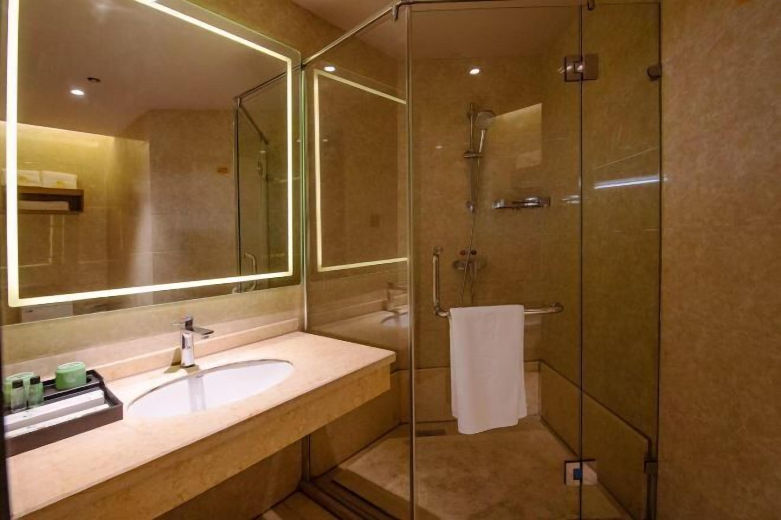 A modern bathroom with a glass-enclosed shower, a large mirror, and a beige countertop with toiletries.