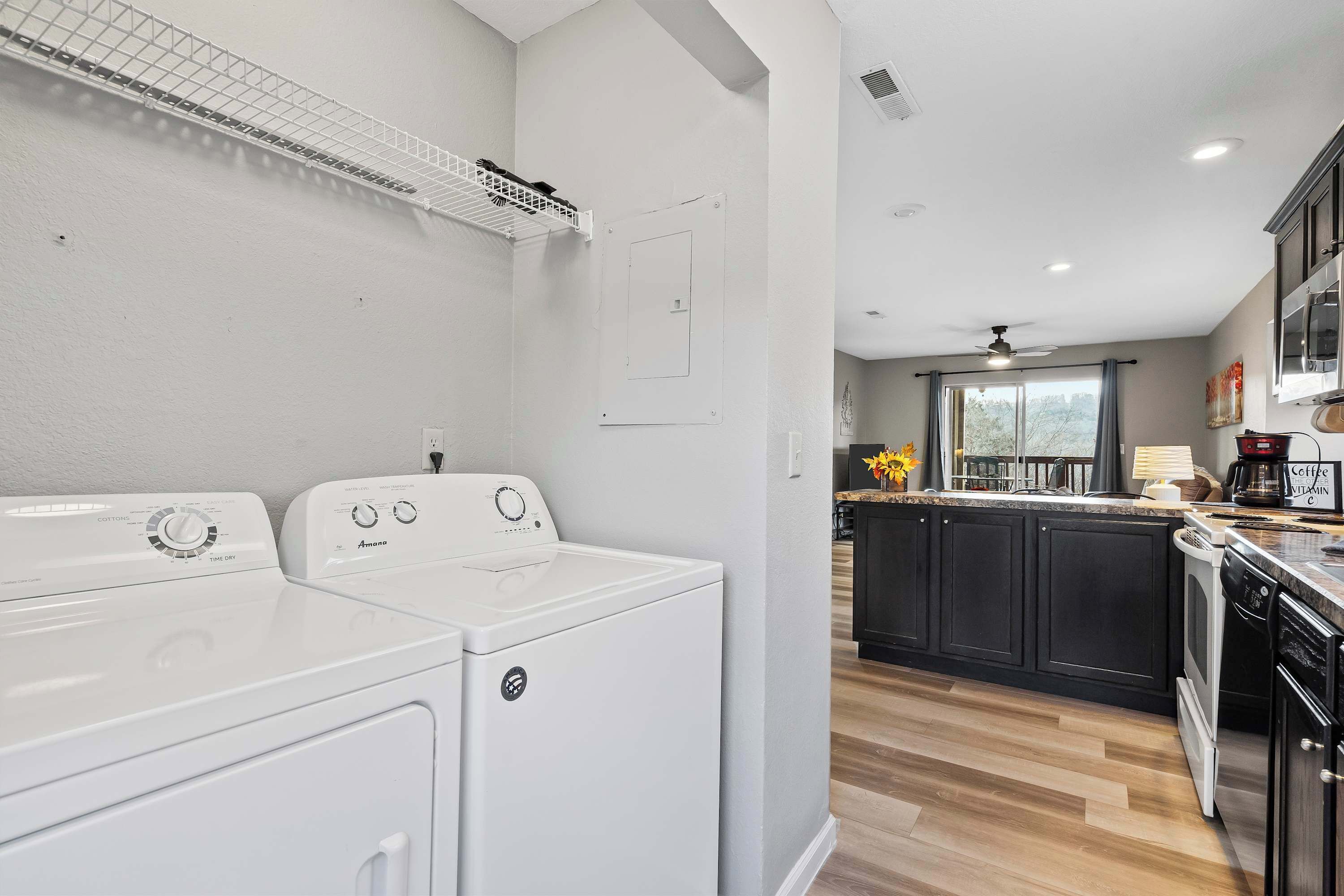 A laundry area with a front-loading washer and dryer, a ceiling fan, and a window with a view of trees.