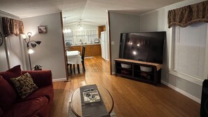Una sala de estar con un sofá rojo, una mesa de centro, un televisor y una cocina al fondo.