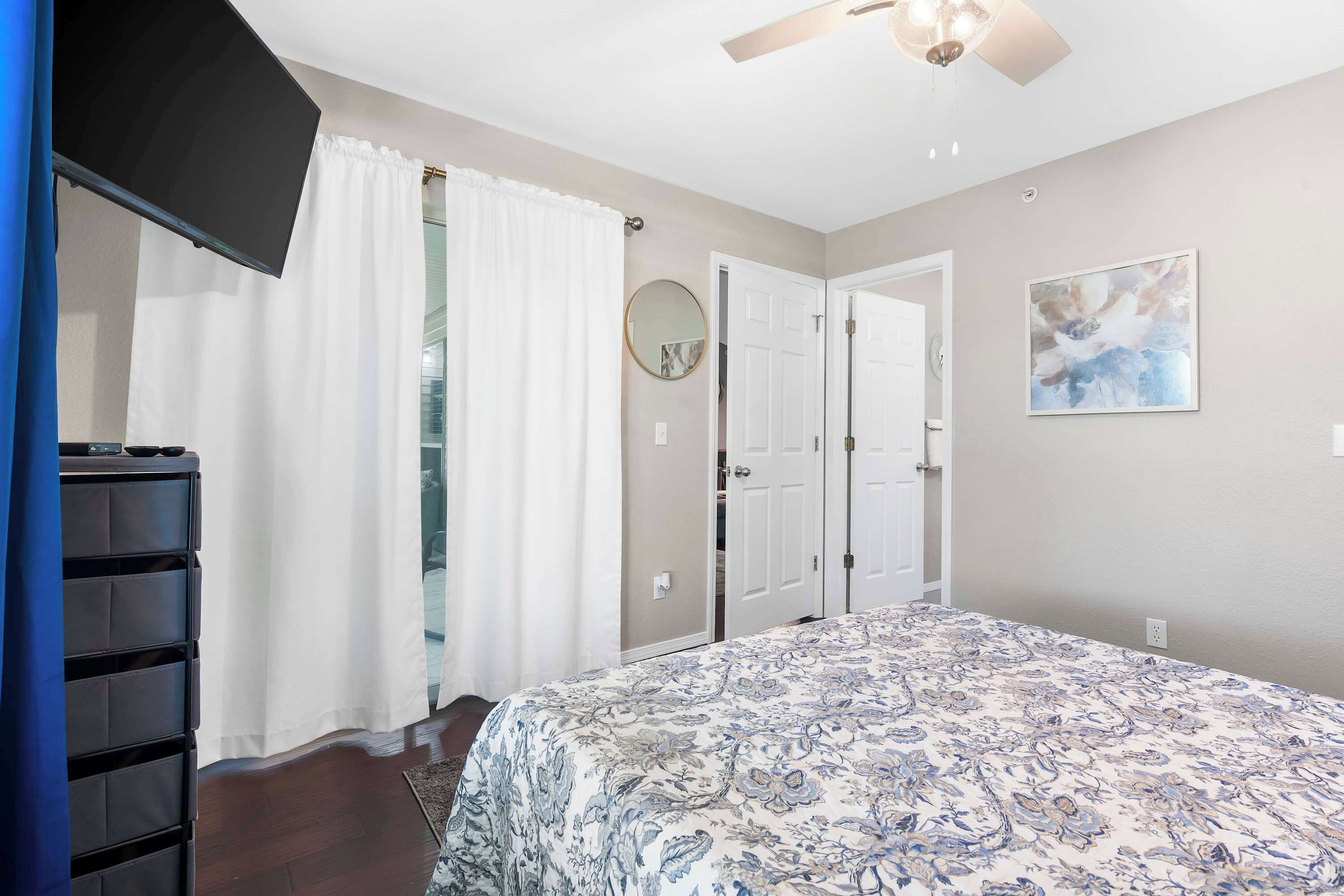 Une chambre à coucher avec un lit, un ventilateur de plafond, une télévision et une armoire.