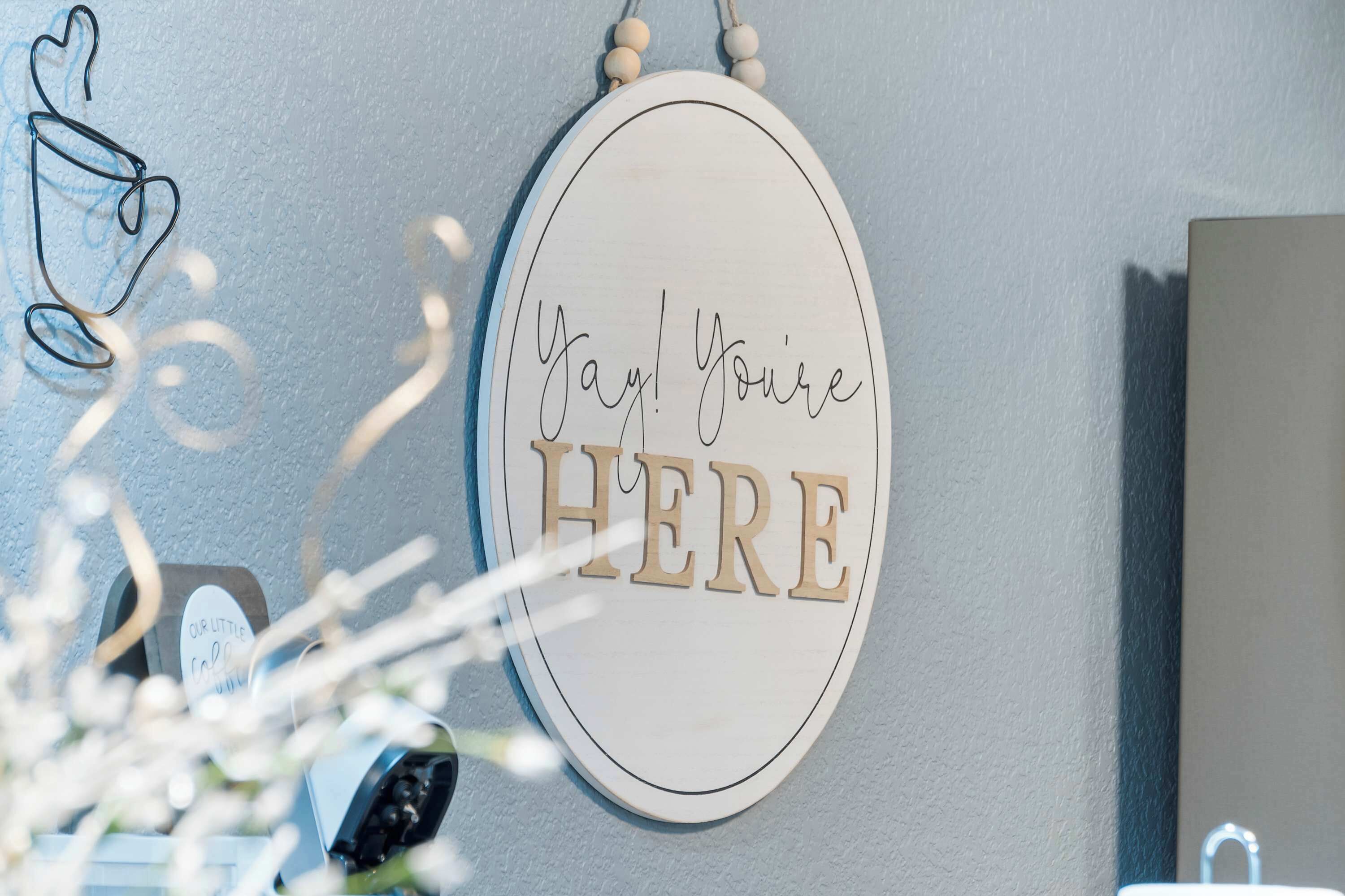 Eine Wand mit einem Schild, auf dem 'Yay! Du bist DA!' steht, und einem dekorativen Gegenstand, der wie ein Brillenpaar aussieht.