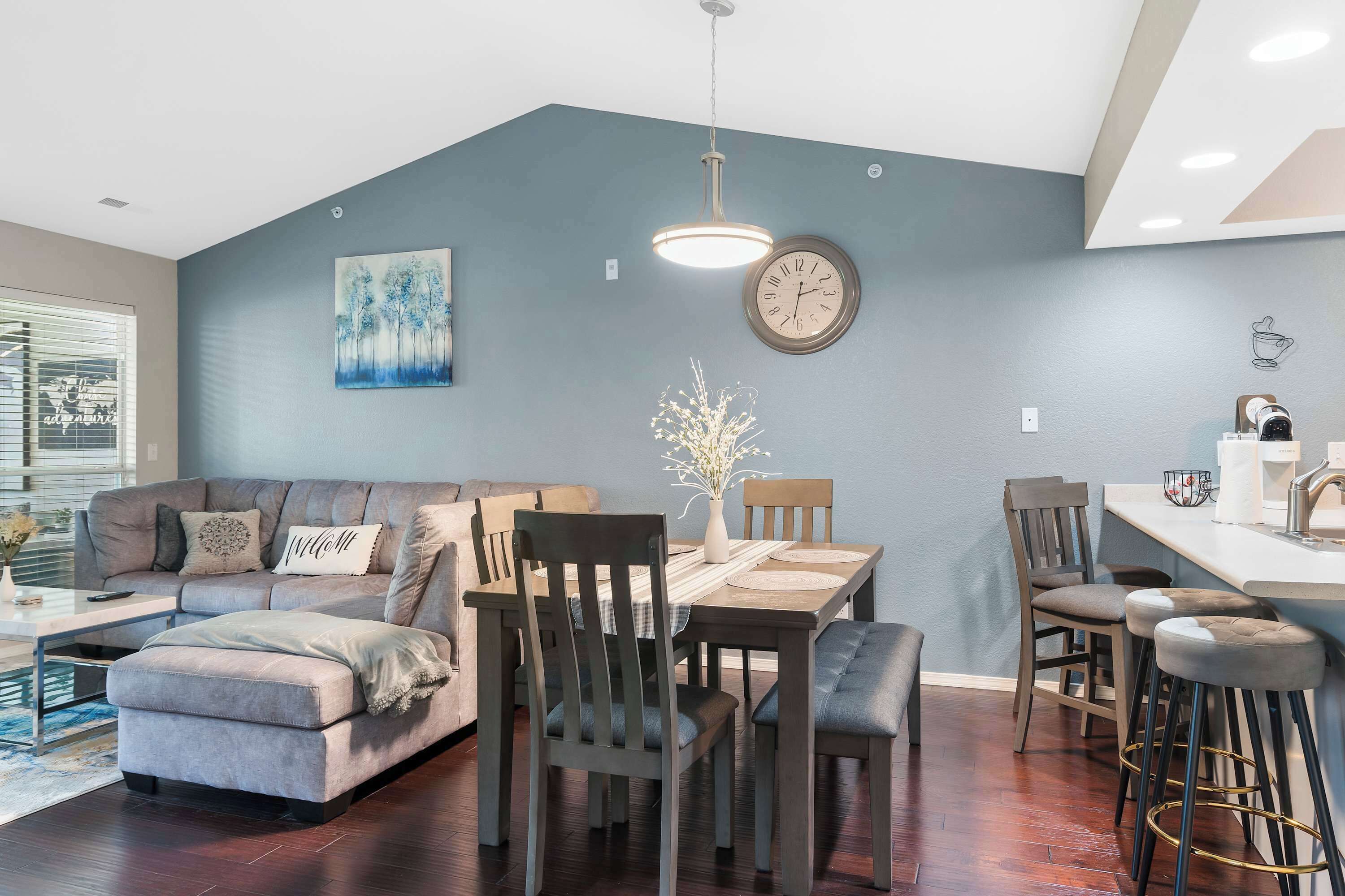 Una sala de estar moderna con sofá, reposapiés y un comedor con sillas y una mesa.