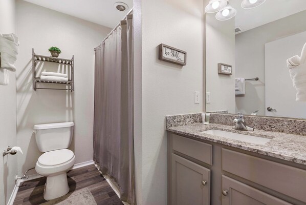 A bathroom with a toilet, a shower curtain, a sink with a mirror, and towel racks.