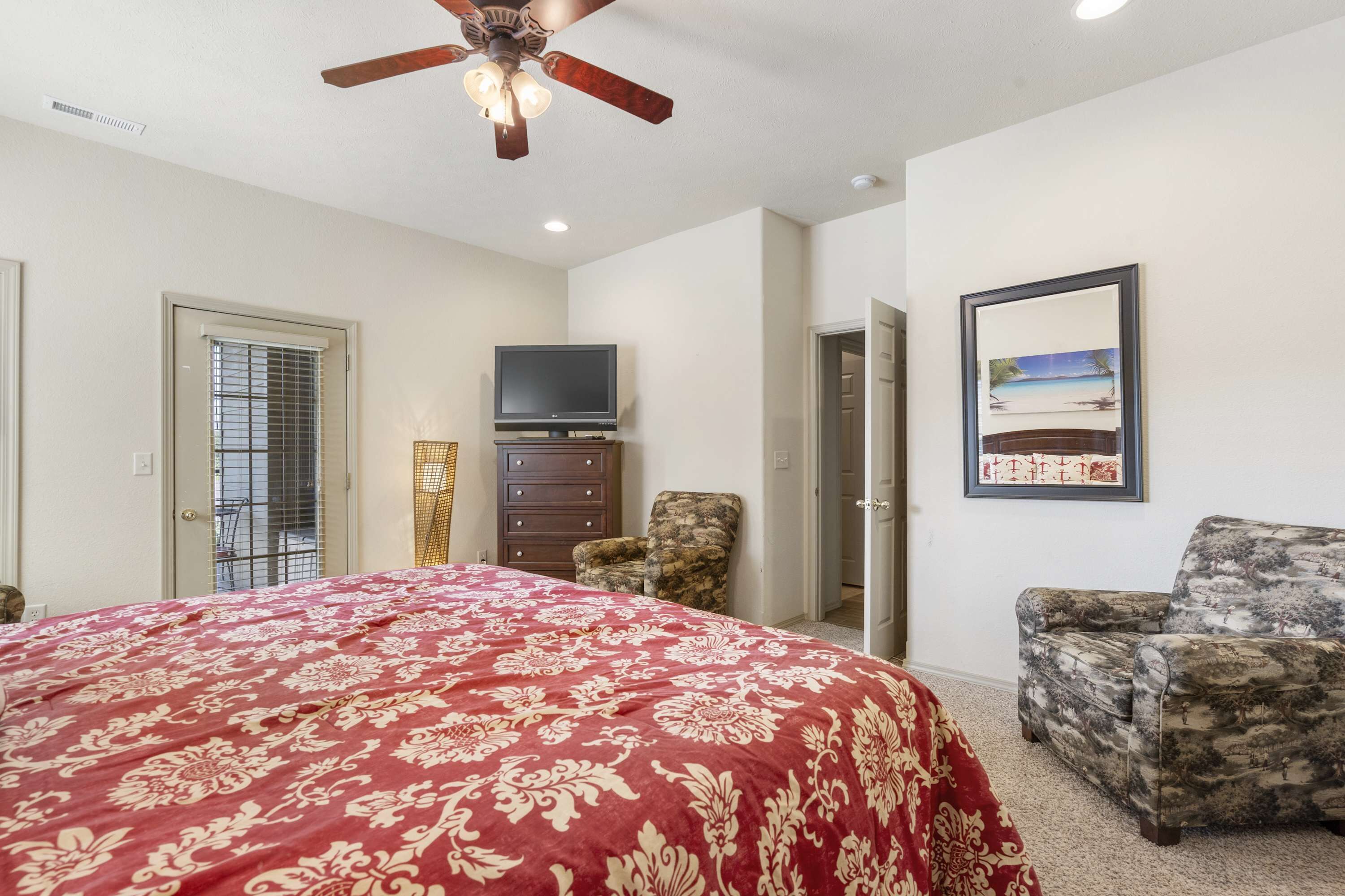 A bedroom with a large bed, a ceiling fan, a television, a chair, and a framed picture on the wall.