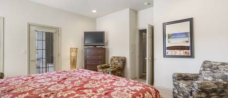 A bedroom with a large bed, a ceiling fan, a television, a chair, and a framed picture on the wall.