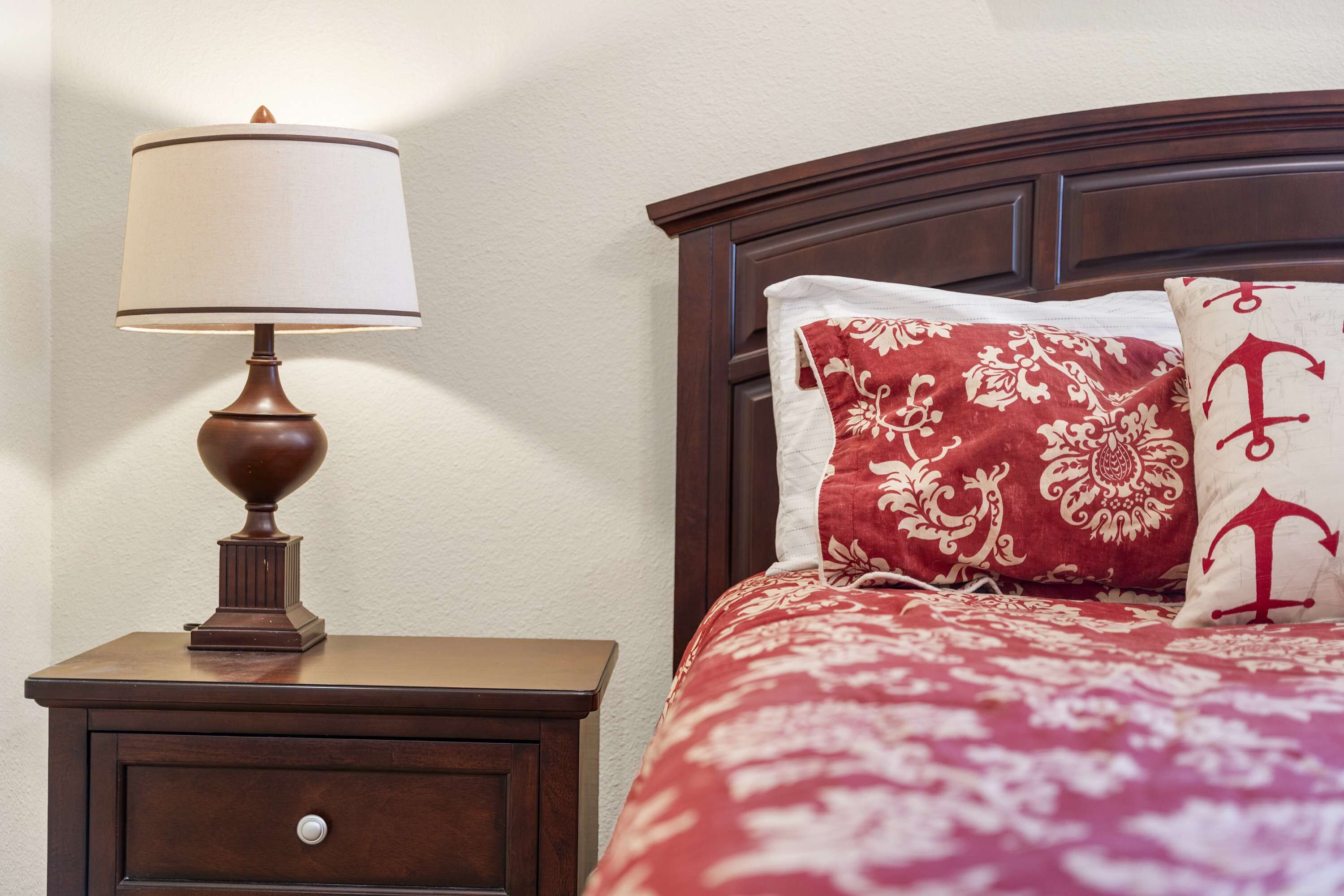 Una cama bien hecha con una colcha de diseño rojo y blanco y dos almohadas, una con una letra 'F' grande.