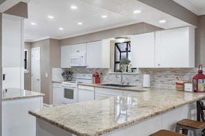 Une cuisine moderne avec des meubles blancs, des plans de travail en granit, un four à micro-ondes, une cuisinière et une fenêtre offrant une belle vue.