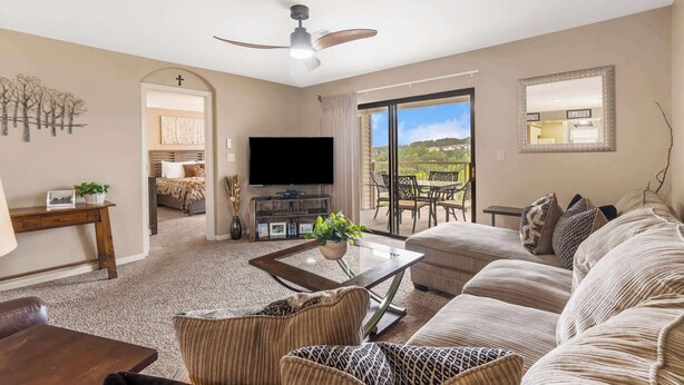 A living room with a sofa, armchairs, a coffee table, a TV, and a balcony with a view. - Golf Course View at the Foothills Resort (Branson)