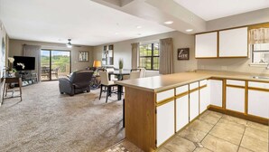 A spacious living area with a dining table, a sofa, and a TV. There is a kitchen with a large island and cabinets. - Golf Course View at the Foothills Resort (Branson)