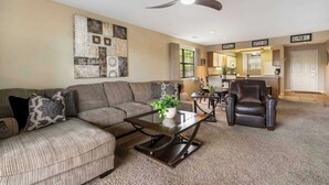 A living room with a sectional sofa, a glass coffee table, a leather armchair, and a ceiling fan. - Golf Course View at the Foothills Resort (Branson)