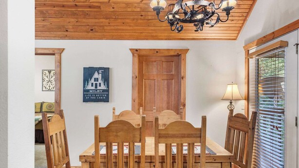 A wooden dining table with six chairs, a wooden ceiling, a chandelier, a wooden door, and a window with blinds. - Milby Hideaway w/ On-site Amenities (Branson West)