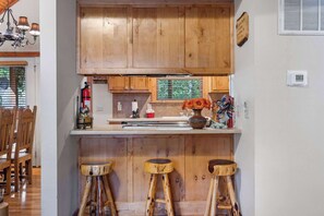 Une cuisine avec des meubles de rangement en bois, un coin bar avec des tabourets et un extincteur.