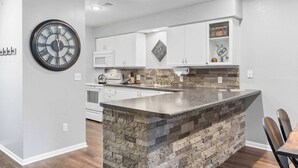 A modern kitchen with a central island, white cabinetry, and a large wall clock.