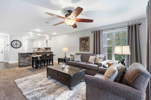 A spacious living room with a dark wooden coffee table, a gray sofa, and a dining area with a stone island and chairs.