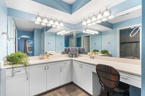 A bathroom with a large mirror, white cabinets, and a shower area.