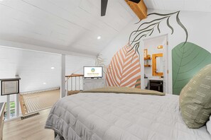 A bedroom with a bed, a television, and a wall with leaf patterns.