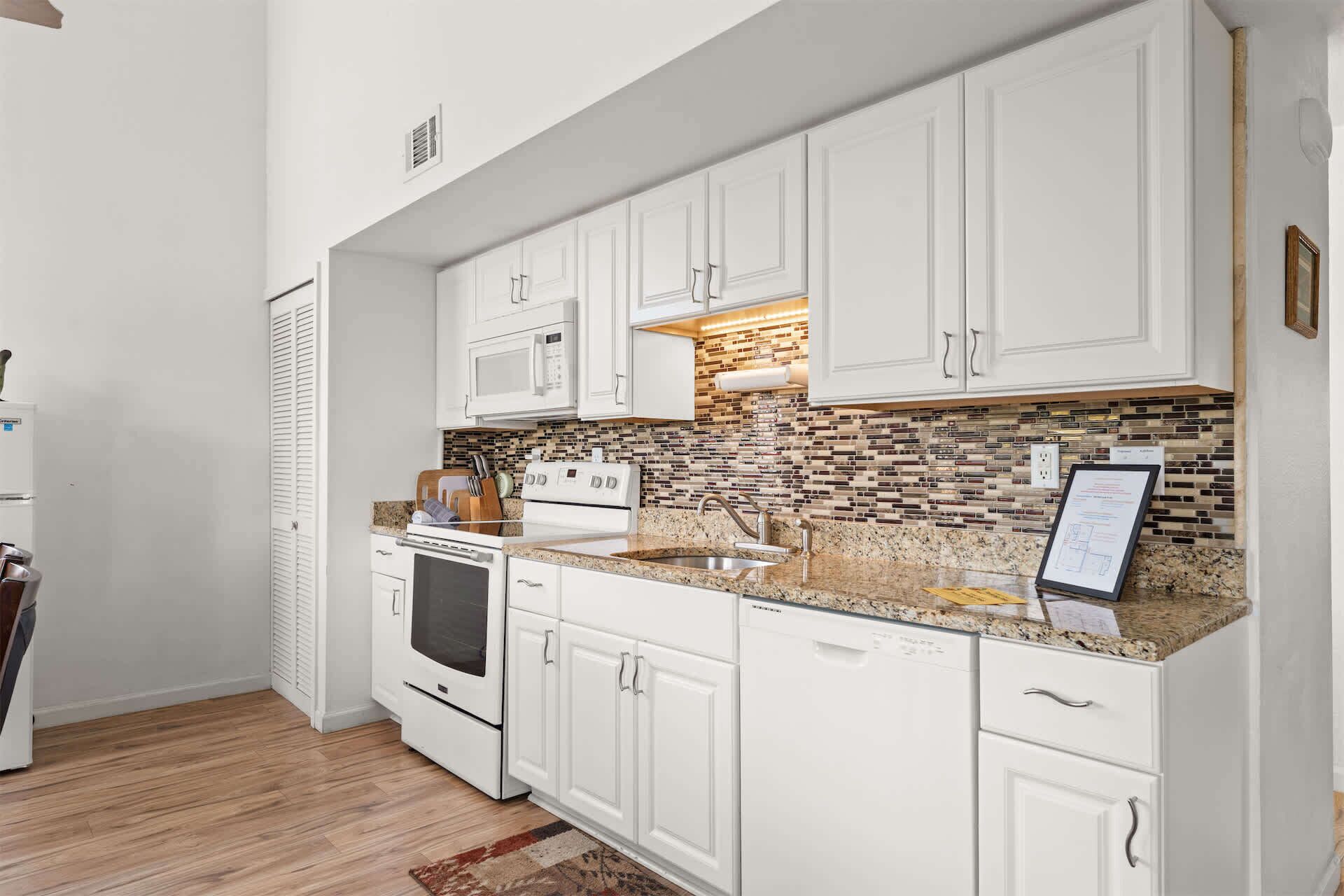 A kitchen with white cabinets, a microwave, stove, and a tiled backsplash.