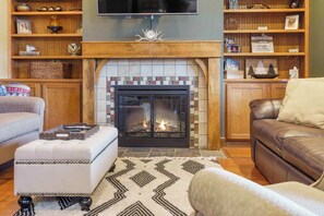 A cozy living room with a fireplace, a television mounted above it, and a bookshelf filled with various items. - Taneycomo Retreat | Lakefront Condo (Branson)