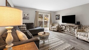 A living room with a sofa, armchairs, a coffee table, a TV, and a large window with curtains.