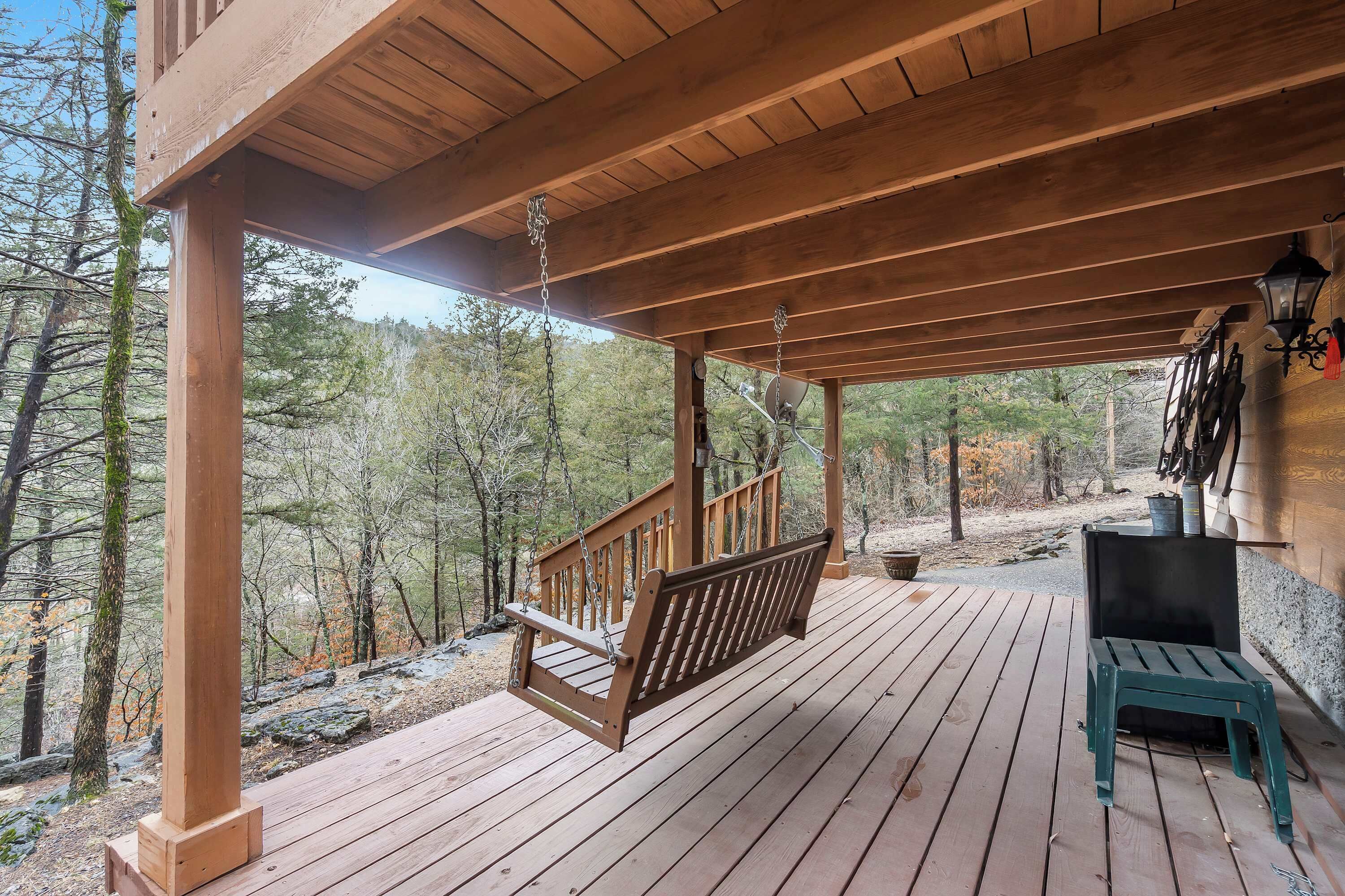 A wooden deck with a swing, a bench, and a stone wall.