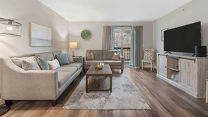 Ein Wohnzimmer mit Sofa, Couchtisch, Fernseher und Blick ins Freie.