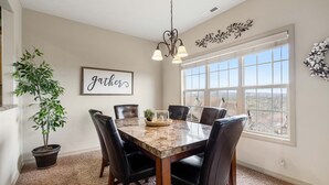 A dining area with a marble table, black chairs, a potted plant, and a window with a view.