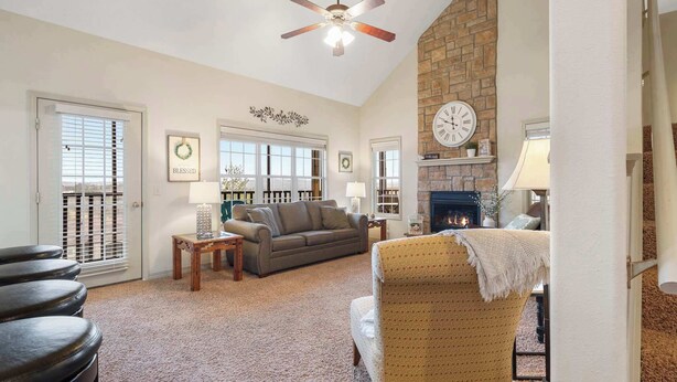 A cozy living room with a fireplace, a ceiling fan, and a large window.