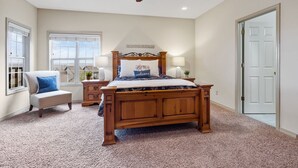 A bedroom with a wooden bed, a chair, a nightstand, a ceiling fan, and a window.