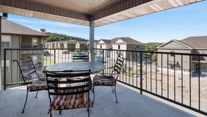 Eine überdachte Terrasse mit rundem Tisch und Stühlen, Blick auf benachbarte Häuser und einen klaren Himmel.