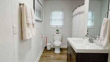 Ein schmales Badezimmer mit Holzboden, weißen Wänden, einer weißen Toilette, einem Waschbecken mit dunklem Schrank und einem Spiegel.