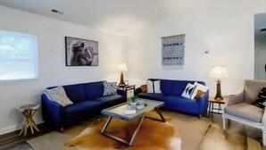 A living room with a blue sofa set, a glass coffee table, and a wooden floor. - Cave Run Lodge Near Lake & Marina Cabin Suite #8 (Morehead)