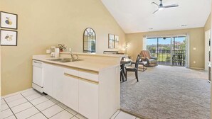 Une cuisine dotée d’un îlot central, un coin repas avec une table et des chaises, et une vue sur un balcon extérieur accessible par une porte-fenêtre coulissante.