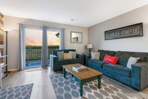 Una sala de estar con un sofá azul, una mesa de centro y vistas a un área exterior a través de una puerta corrediza.