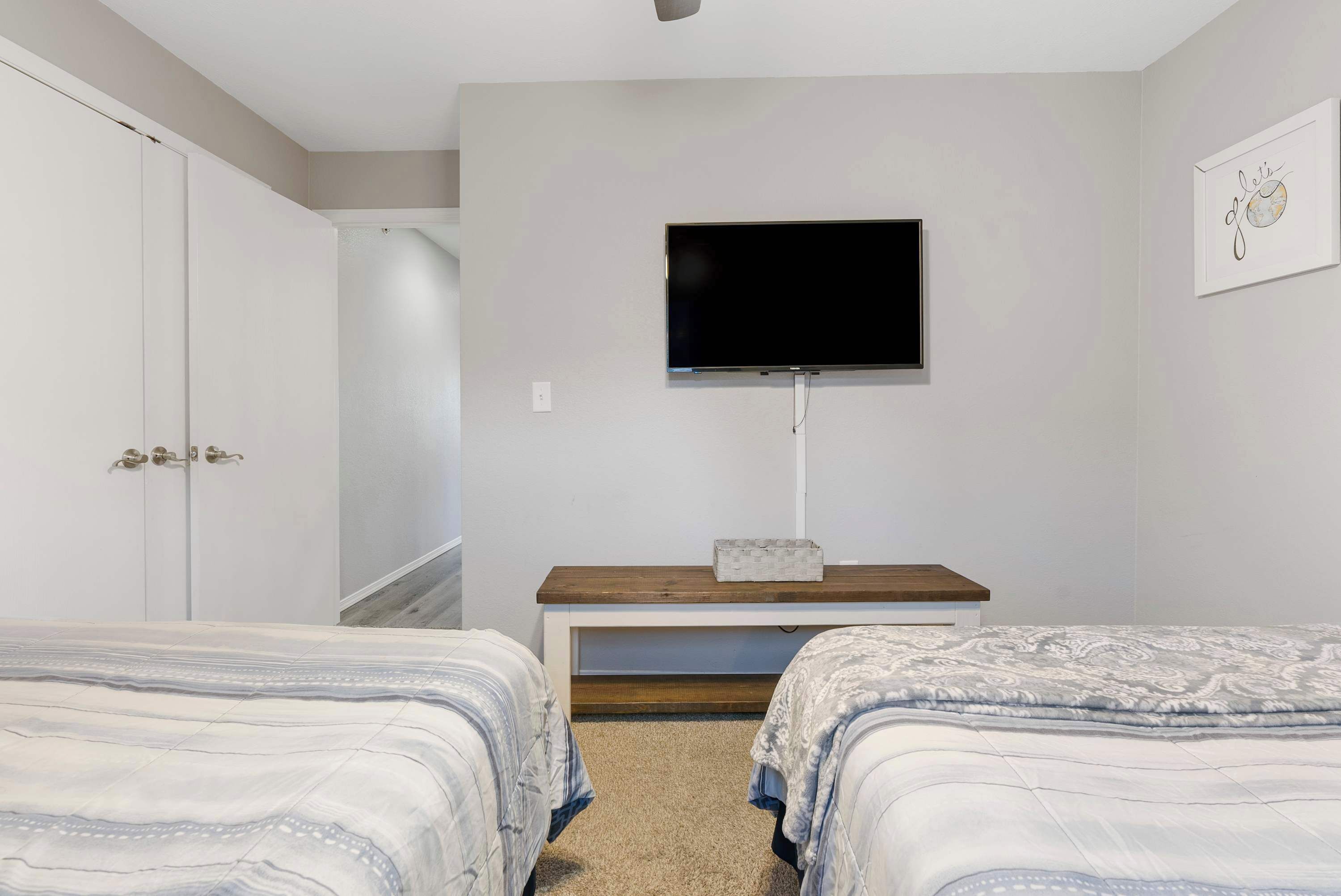 Un dormitorio con dos camas, un televisor montado en la pared, un banco de madera y un armario.