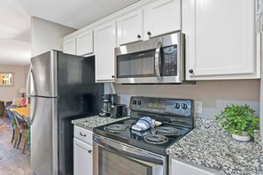 Una cocina con electrodomésticos de acero inoxidable, gabinetes blancos, encimeras de granito y una zona de comedor con mesa y sillas.