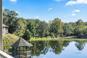 A tranquil lakeside view with a gazebo, trees, and a distant building. - Vansen's Golfshores – Inviting, Cozy Condo on Golf Course! (Branson)