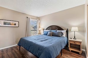 Une chambre à coucher avec un lit, des tables de chevet, une fenêtre avec des rideaux et un tableau encadré au mur.