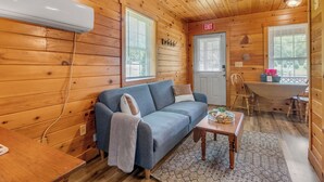 L’intérieur d’un chalet en bois, avec un canapé, une petite table, une table à manger et un panneau indiquant la sortie.