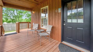 Une terrasse en bois avec des chaises et une table, une porte noire avec un numéro, et une vue sur les arbres.