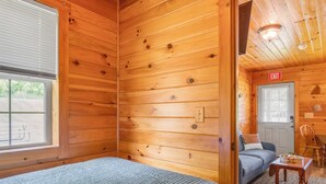 L’intérieur d’un chalet en bois, avec un lit, un canapé, une table à manger et un panneau indiquant la sortie.