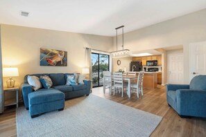 A living room with a sofa, ottoman, and dining table with chairs. There is a kitchen area with a refrigerator and microwave. - Lakeview At Table Rock (Kimberling City)