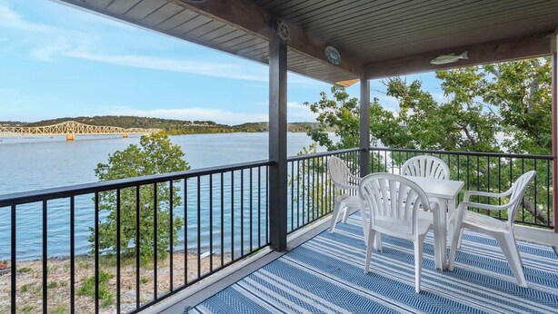 A covered outdoor area with a table and chairs, overlooking a body of water and a bridge. - Lakeview At Table Rock (Kimberling City)