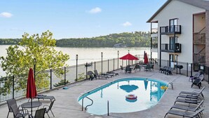 A pool area with lounge chairs and umbrellas, a view of a lake, and a building with balconies. - Lakeview At Table Rock (Kimberling City)