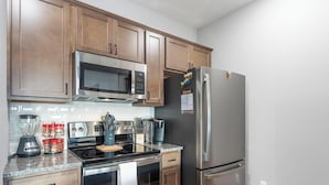 A kitchen with wooden cabinets, a stainless steel refrigerator, a microwave, a stove, and a coffee maker. - Two Pines – Endless Views and Attractions! (Branson)