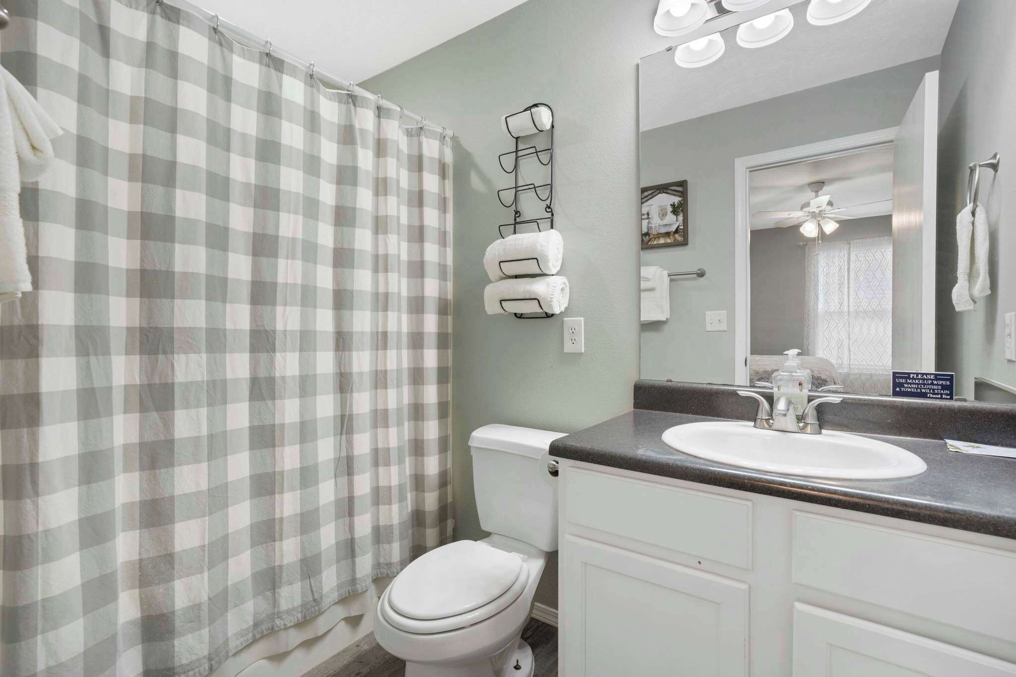 A bathroom with a checkered shower curtain, a toilet, a sink with a mirror, and a towel rack.