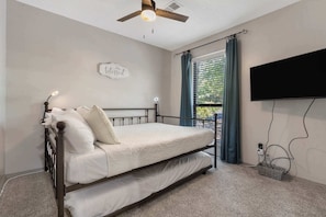 Ein Schlafzimmer mit Bett, Deckenventilator, Wand-Fernseher und einem Fenster mit Vorhängen.